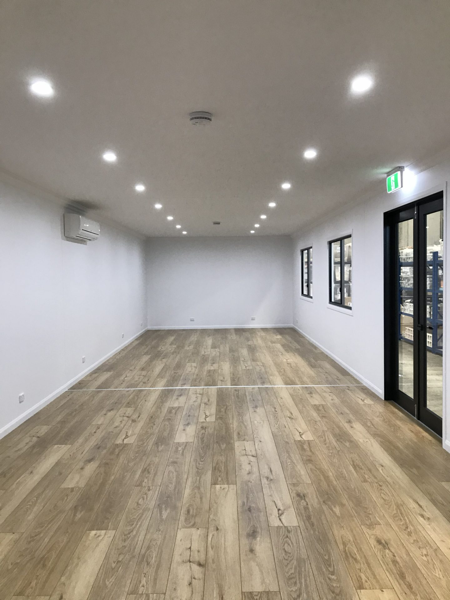 Finished open office interior with timber-look flooring, downlights and glazed doors