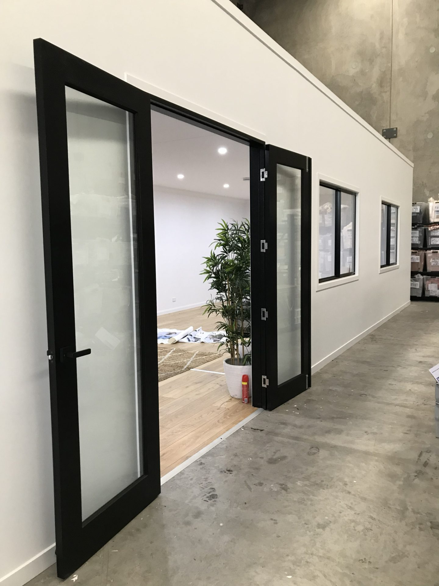 Framed and lined office within a warehouse, black-framed glazed doors